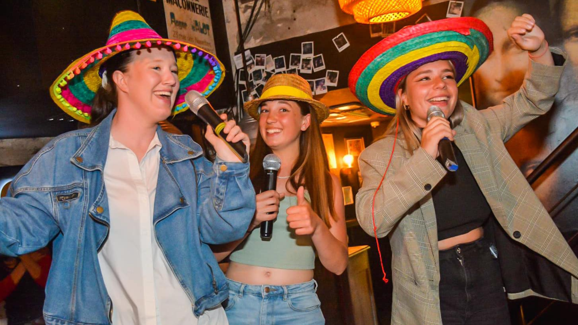 Karaoké Les Sables d'Olonne. 3 jeunes femmes chantent au micro. Elles portent un chapeau mexicain rose vert et jaune.